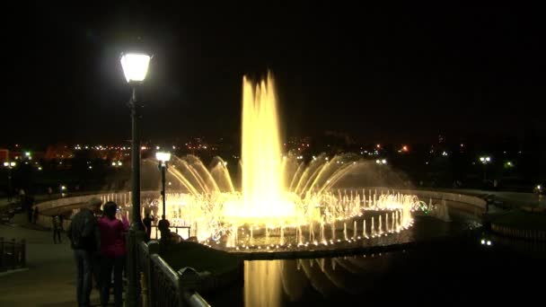 Menschen spazieren nachts in der Nähe tanzender Brunnen. — Stockvideo