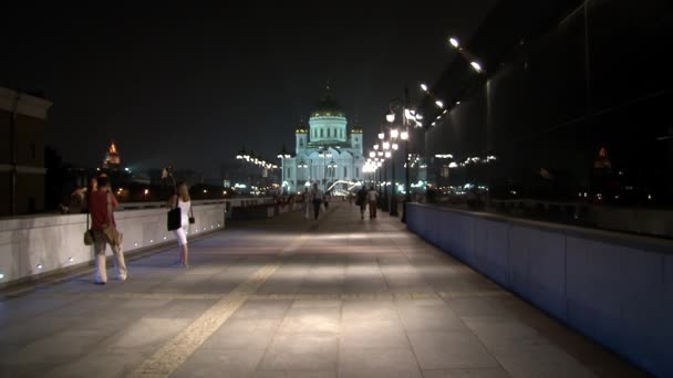 People walk along Patriarchal bridge to Cathedral of Christ Savior at night. — Stock Video