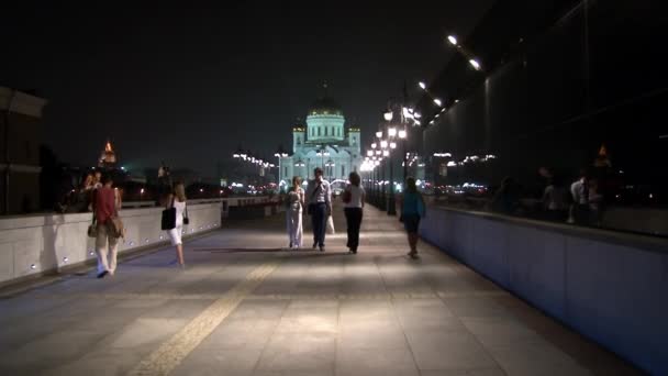 People walk along Patriarchal bridge to Cathedral of Christ Savior at night. — Stock Video