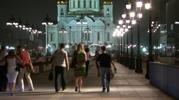 La gente cammina lungo il ponte patriarcale fino alla Cattedrale di Cristo Salvatore di notte . — Video Stock