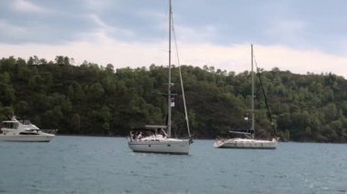 Mavi denizin arka planında beyaz yatlar ve gökyüzünde bulutlar.