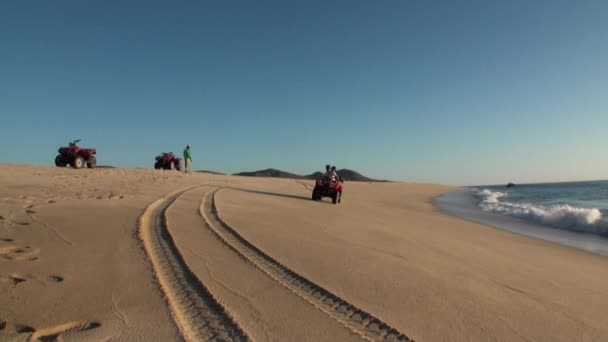 Zespół turystów jeździ quadem wzdłuż piaszczystego brzegu i macha powitaniem. — Wideo stockowe