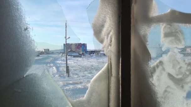 Nieve en una rota ventana congelada de casa abandonada en ciudad desierta . — Vídeos de Stock