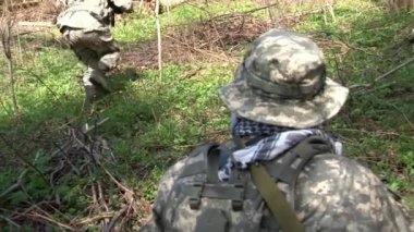 Askerî üniformalı adamlar ormanda hava yumuşaklığıyla askeri poligon oynuyorlar..