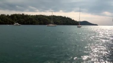 Mavi denizin arka planında beyaz yatlar ve gökyüzünde bulutlar.