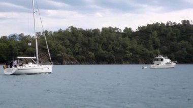 Mavi denizin arka planında beyaz yatlar ve gökyüzünde bulutlar.