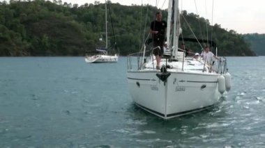 Mavi denizin arka planındaki beyaz yatlardaki insanlar ve gökyüzündeki bulutlar..