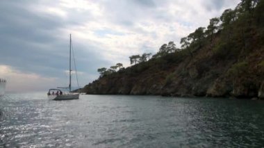 Mavi denizin arka planında beyaz bir yat ve gökyüzünde bulutlar.