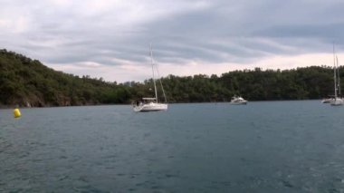 Mavi denizin arka planındaki beyaz yatlardaki insanlar ve gökyüzündeki bulutlar..