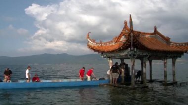 Fuxian Gölü 'nde Çin usulü çatısı olan Çin teknesi çardağındaki insanlar..