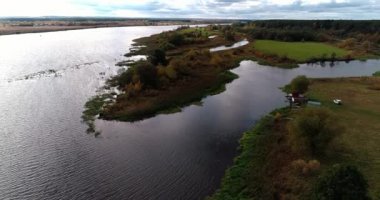 Arka planda gökyüzü ve çarpıcı manzara manzaralı bulutlarla çevrili bir nehir üzerinde evleri ve bahçeleri olan kırsal arazi aracı video panoraması. Açık hava iklimi kavramı.