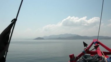 Siyah bayraklı ve mavi ipli kırmızı gemi pruvası denizin arka planında hareket ediyor.