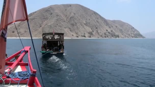 Muž sedí v pohybující se lodi s červenou přídí lodi a černou vlajkou na moři. — Stock video