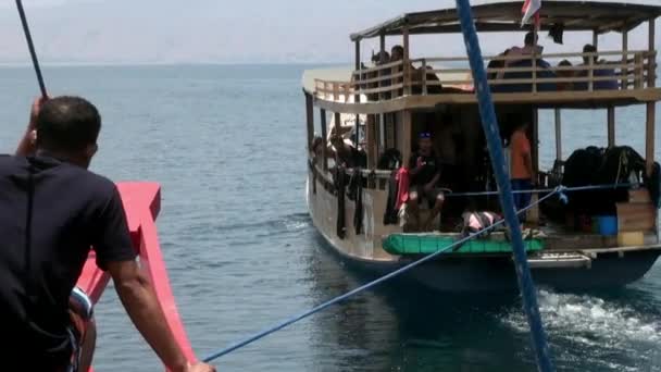 Человек сидит в движущейся лодке с красным носом корабля и черным флагом в море. — стоковое видео