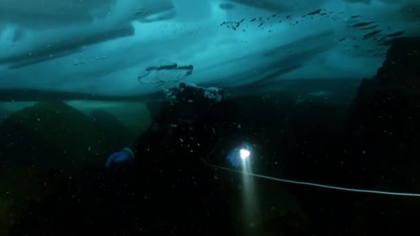 Caméraman sous-marin avec caméra et plongeur technique sous la glace du lac Baïkal. — Video