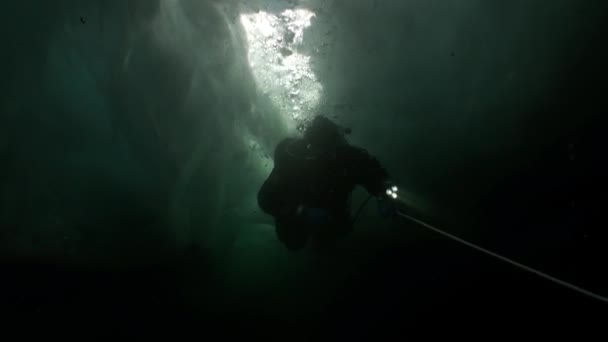 Underwater cameraman with camera and technical diver under ice of lake Baikal.
