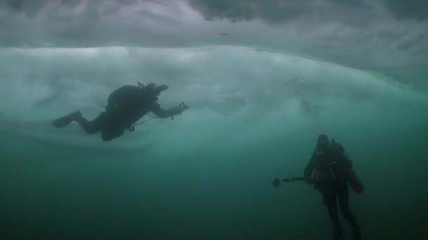 Duiker onder turkoois ijs met onderwater cameraman in het Baikalmeer. — Stockvideo