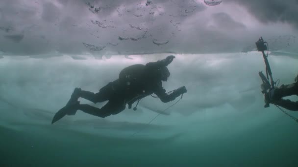 Caméraman sous-marin avec caméra et plongeur technique sous la glace du lac Baïkal. — Video