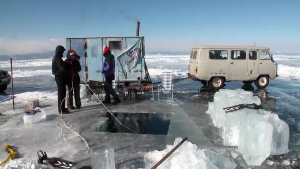 Lidé zahřívají silniční saunu v blízkosti velkých ledových bloků a ledových děr na Bajkalu. — Stock video