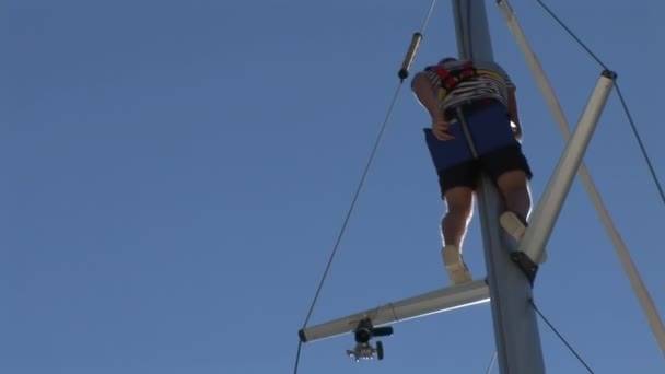 Man stijgt op mast van jacht op de achtergrond van blauwe lucht en zon . — Stockvideo