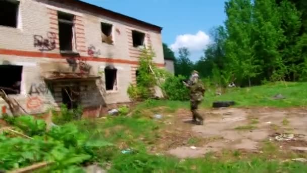 Airsoft speler in militair uniform met wapen schieten in de buurt van geruïneerd huis. — Stockvideo