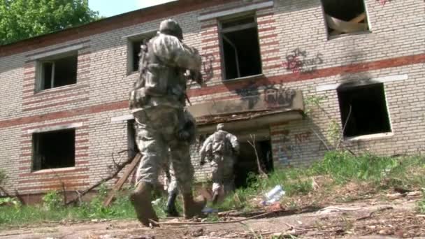 Airsoft player in military uniform with weapon near ruined house. — Stock Video