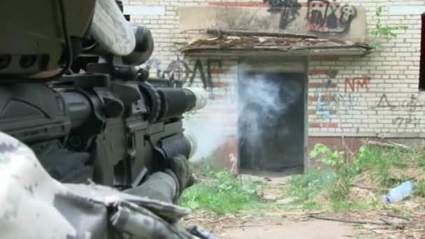 Airsoft player in military uniform with weapon shoots near ruined house. — Stock Video