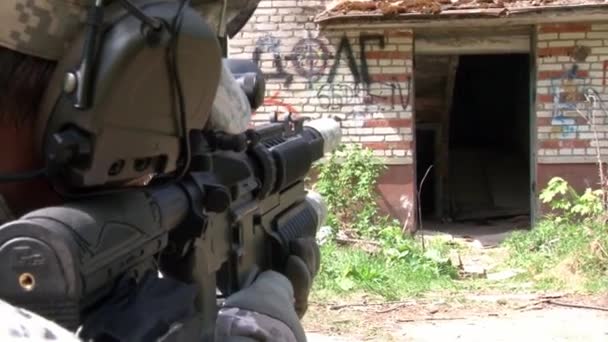 Airsoft player in military uniform with weapon shoots near ruined house. — Stock Video