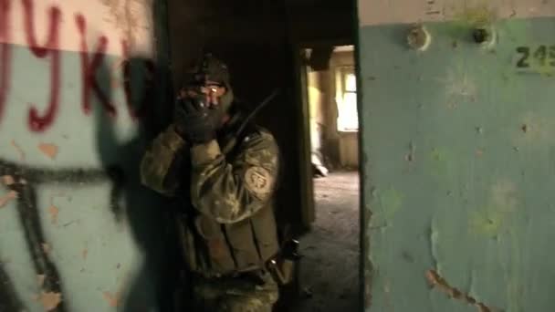 Airsoft player in military uniform with weapon in ruined house. — Stock Video