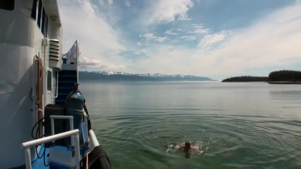 Man swims near the ship in clear transparent water of Lake Baikal. — стокове відео