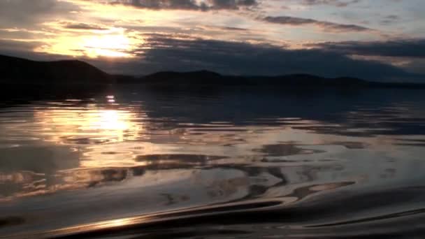 Golven op het wateroppervlak op de achtergrond van donkere lucht en grijze wolken bij zonsondergang. — Stockvideo