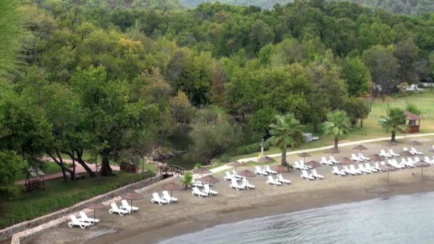 Liegestühle in der Nähe von grünen Bäumen am Strand des Mittelmeeres in der Türkei. — Stockvideo
