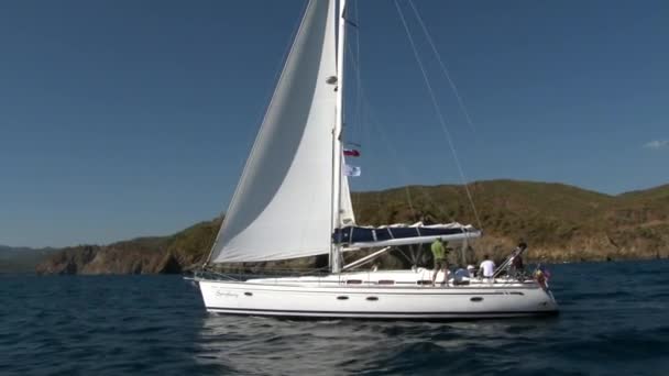 人々はトルコの山の海岸を背景に白いヨットに乗って航海します. — ストック動画