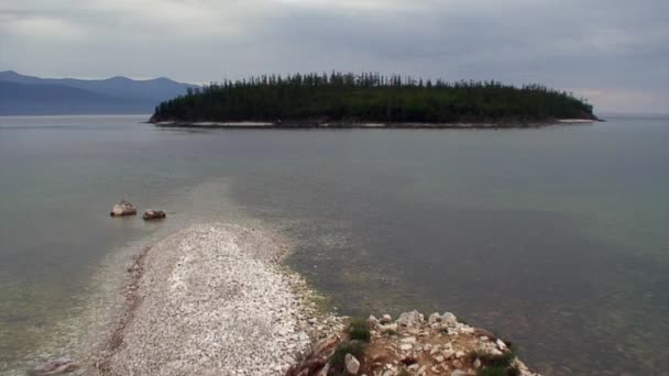 Ostrov se zelenými stromy na pozadí skalnatého pobřeží jezera Bajkal. — Stock video