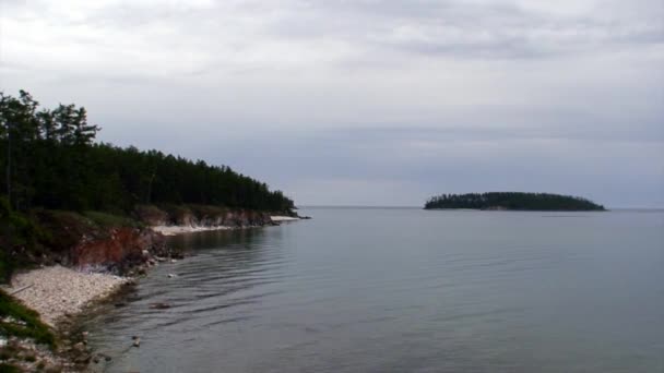 Île aux arbres verts sur fond de littoral rocheux du lac Baïkal.