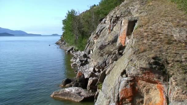 Oranje rode rotsen op de kustlijn van het diepste zoetwatermeer Baikal. — Stockvideo