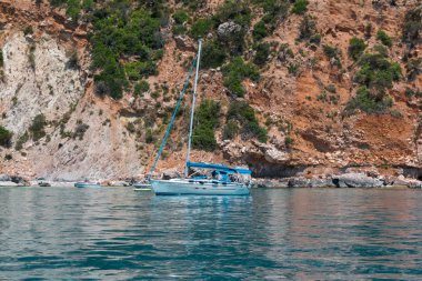 Beyaz yelkenli demirlemiş sakin deniz ve görkemli kaya backg