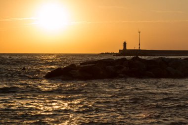 Fener, resif ve günbatımı dalgalı denizde silüeti