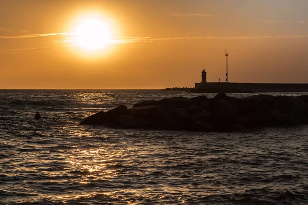 Silhouette von Leuchtturm, Riff und abgehacktem Meer bei Sonnenuntergang — Stockfoto
