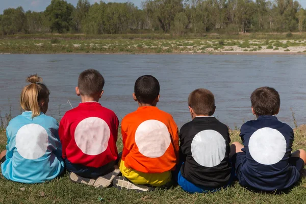 Dzieci w kolejce odwrócił się z koszule z różnych kolorach siedzących na skraju rzeki — Zdjęcie stockowe