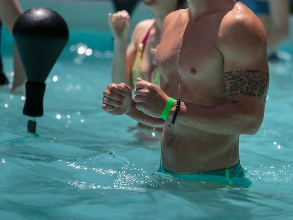 Ragazzo che fa aerobica in acqua con pallone da boxe in una piscina all'aperto — Foto Stock