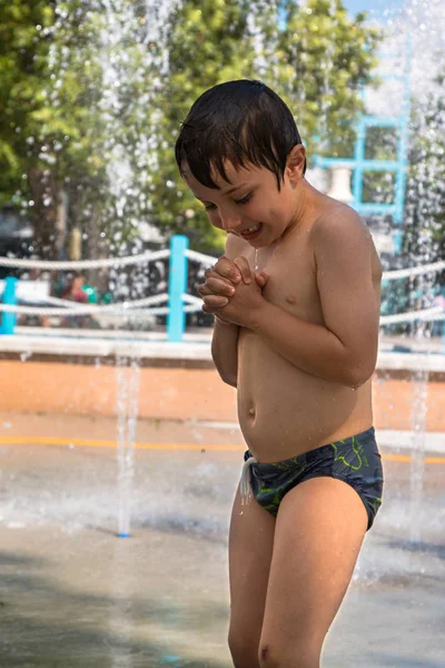 Boldog fiú játszik a vízben a szökőkút nyári idő-ban közterület — Stock Fotó