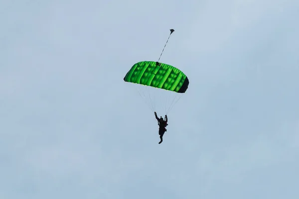 Парашютист с зеленым парашютом против чистого голубого неба — стоковое фото