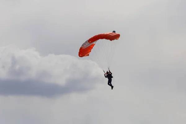 Парашютист с оранжевым парашютом против чистого голубого неба — стоковое фото