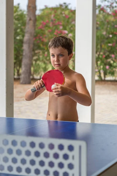 Zehnjähriger Junge spielt ohne Hemd Tischtennis im Park. — Stockfoto