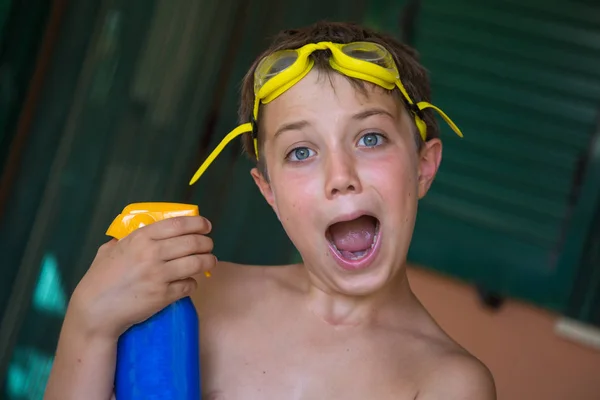 Junge mit gelber Schwimmbrille spielt mit Sonnenschutzflasche — Stockfoto