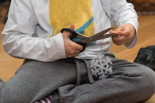 Мальчик, использующий металлические ножницы, чтобы перерезать ленту декоративного рождественского объекта — стоковое фото