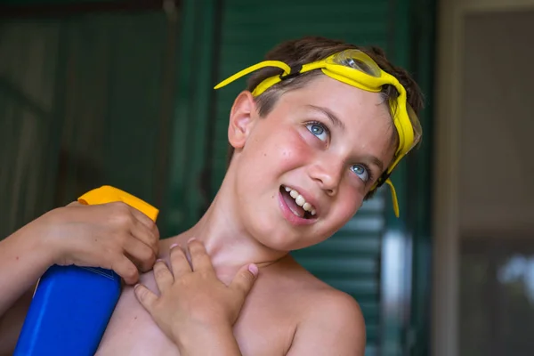 Junge mit gelber Schwimmbrille spielt mit Sonnenschutzflasche — Stockfoto