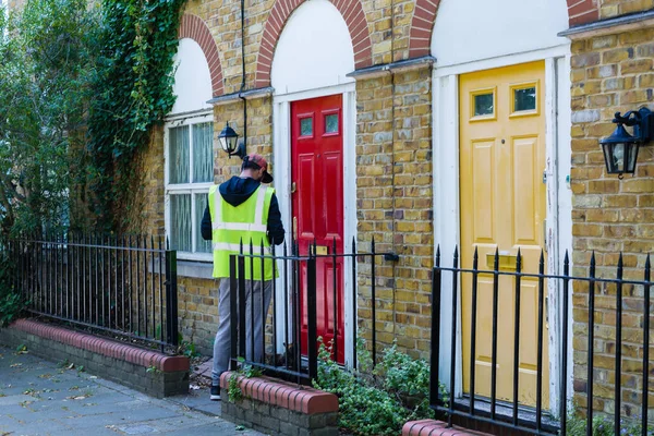 Mensajero con gorra y babero amarillo Fuera de una puerta de una casa en la planta baja para una entrega — Foto de Stock