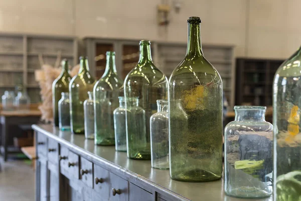 Six Green, Empty and Dirty Glass Bottles over an Antique Wooden Chest of Drawers.